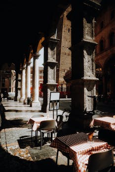 Sunlit Italian cafe scene with checkered tablecloths under historic arches.