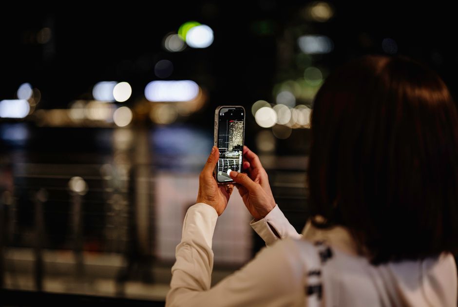 A person photographs Bangkok's vibrant night cityscape using a mobile phone.