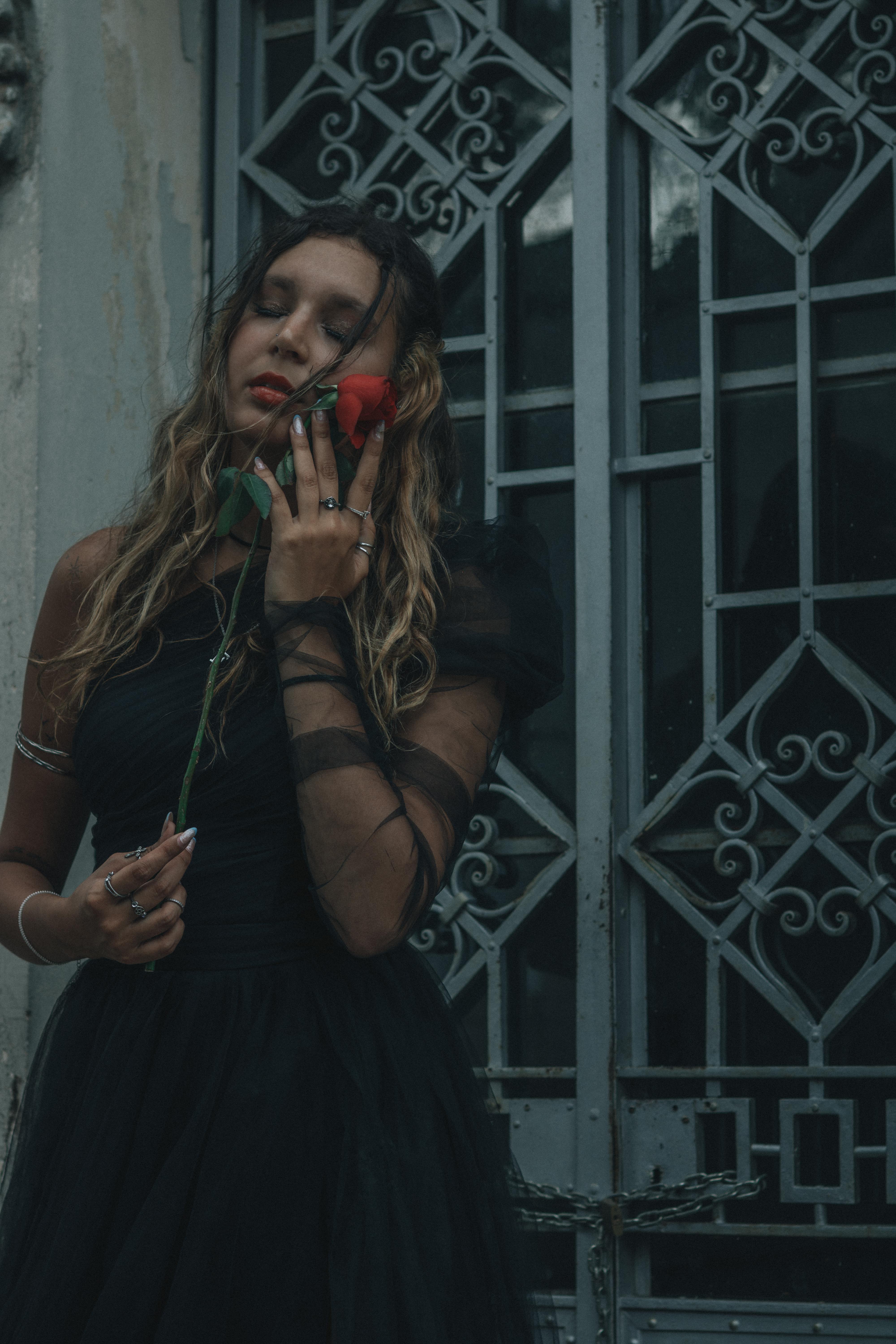 Zadarmo Dramatický portrét ženy v čiernych šatách držiacej ružu pri zdobenej bráne. Fotka z fotobanky
