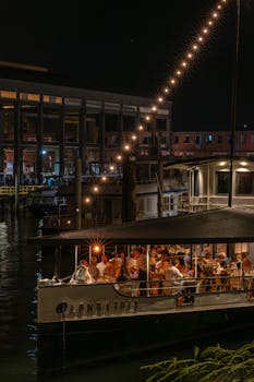 Enjoy an evening dinner on a boat with warm lights and city backdrop.