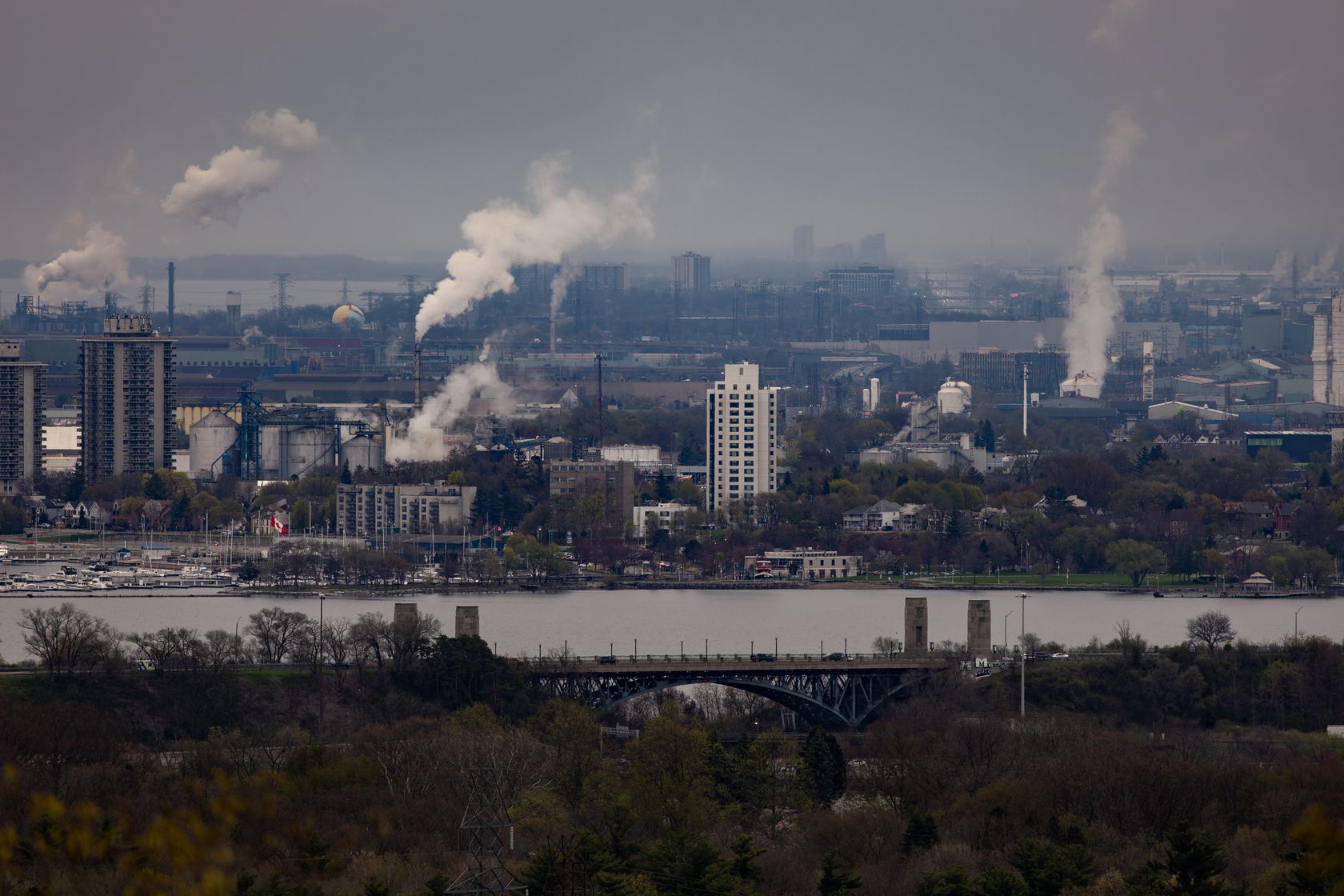 Urban landscape showing factories with smoke and a bridge over water.