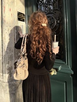 Woman with curly hair wearing a black dress standing at a doorway and holding a drink.