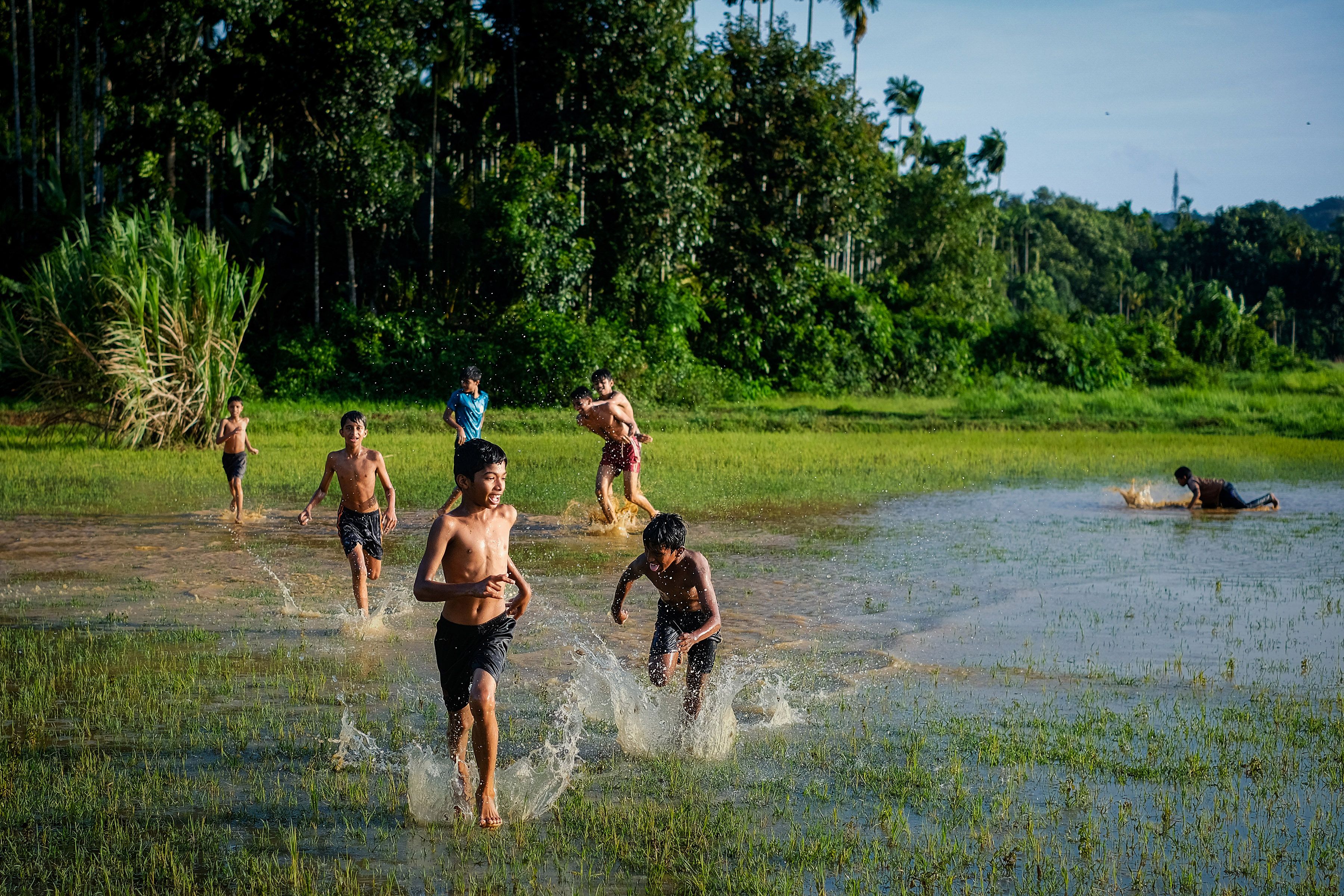 Group of children having fun in a watery field under the sun in South India.