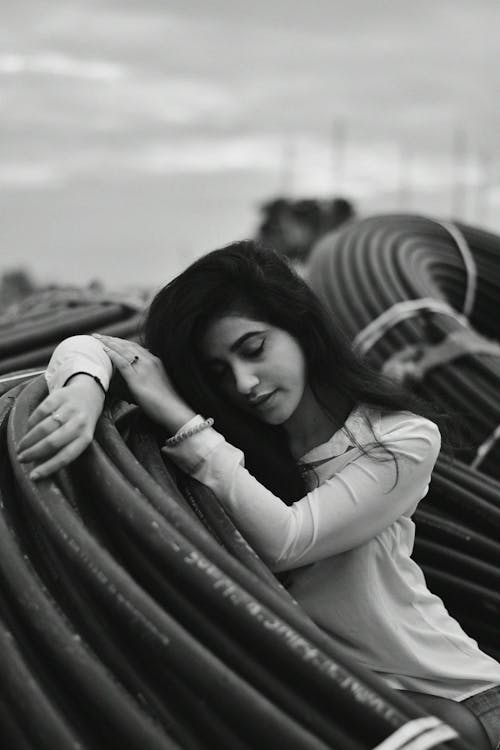 Grayscale Photo of Woman Lying on Roll of Pvc Pipes