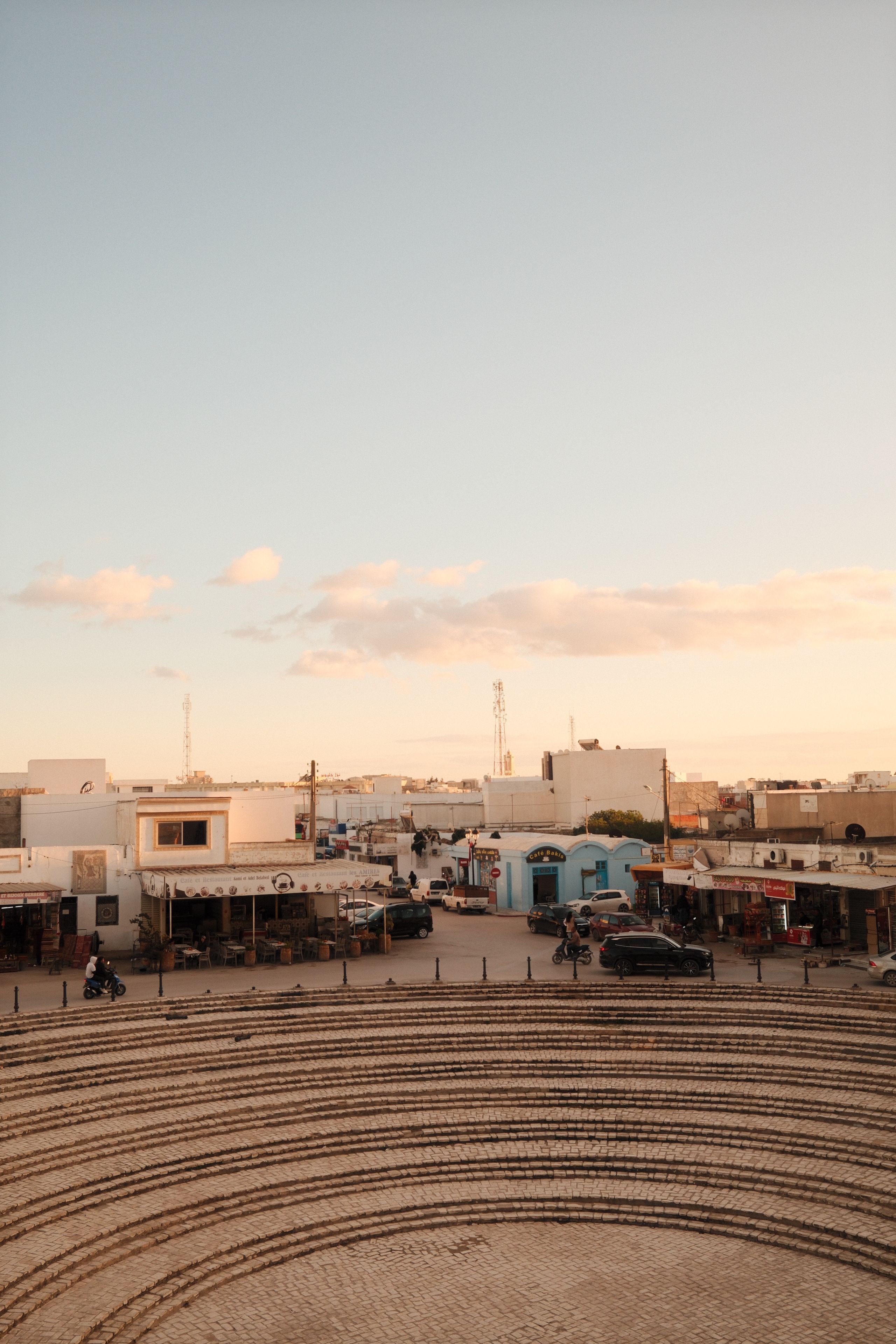 View of El Jem scene with amphitheater and village buildings illuminated by sunset glow.