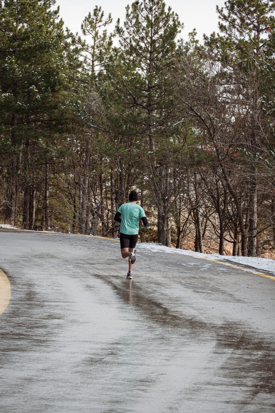 Runner on a wet grey road through winter pines — photo by Emre Gokceoglu from Pexels