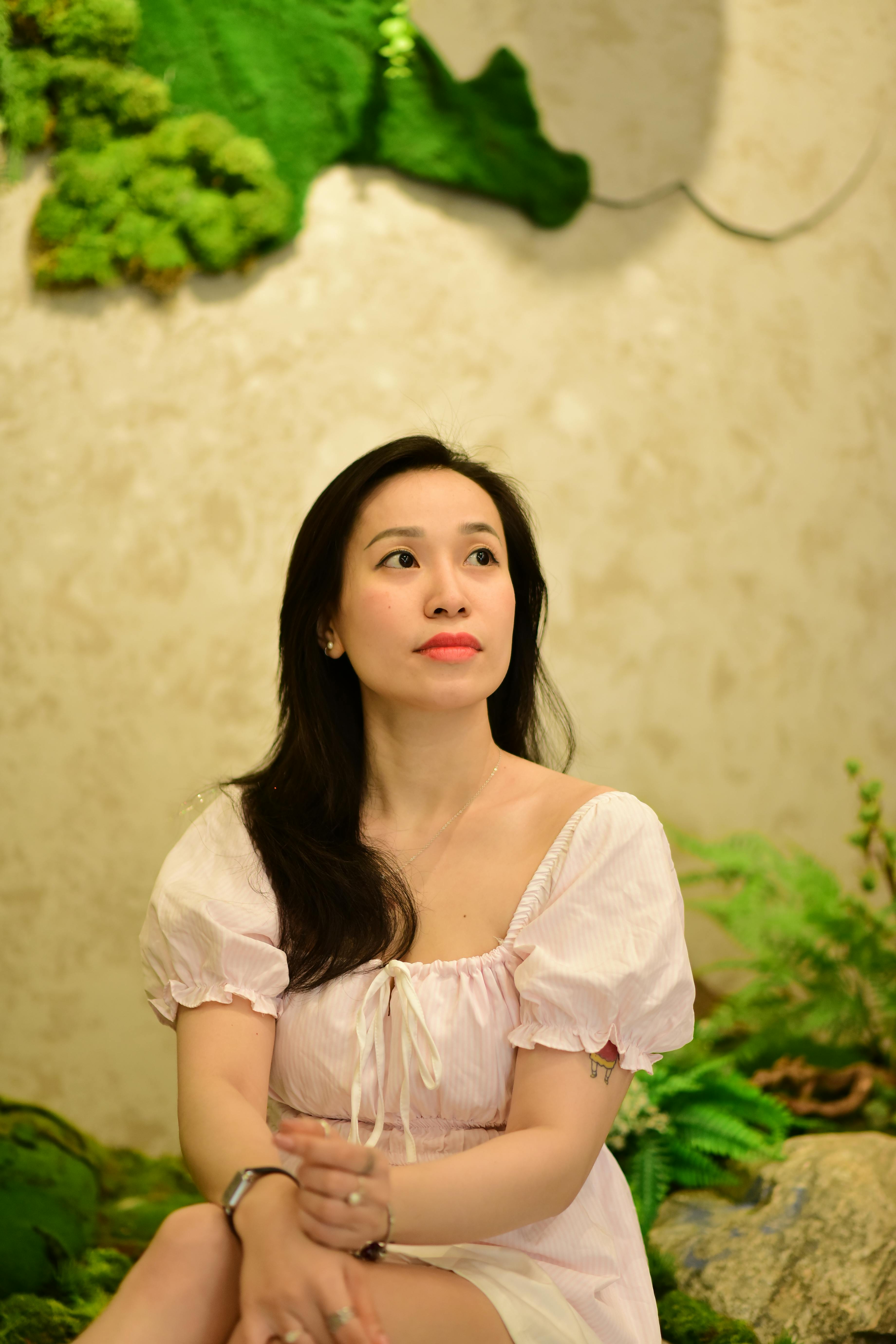 A serene portrait of a woman in a lush indoor garden setting with bright lighting.