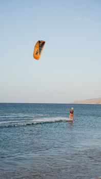 Kiteboarder enjoying the ocean under clear skies with a vibrant orange kite.