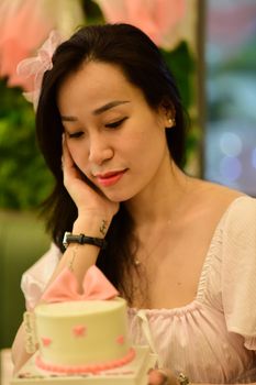 A young woman contemplating a birthday cake in a cozy indoor setting.