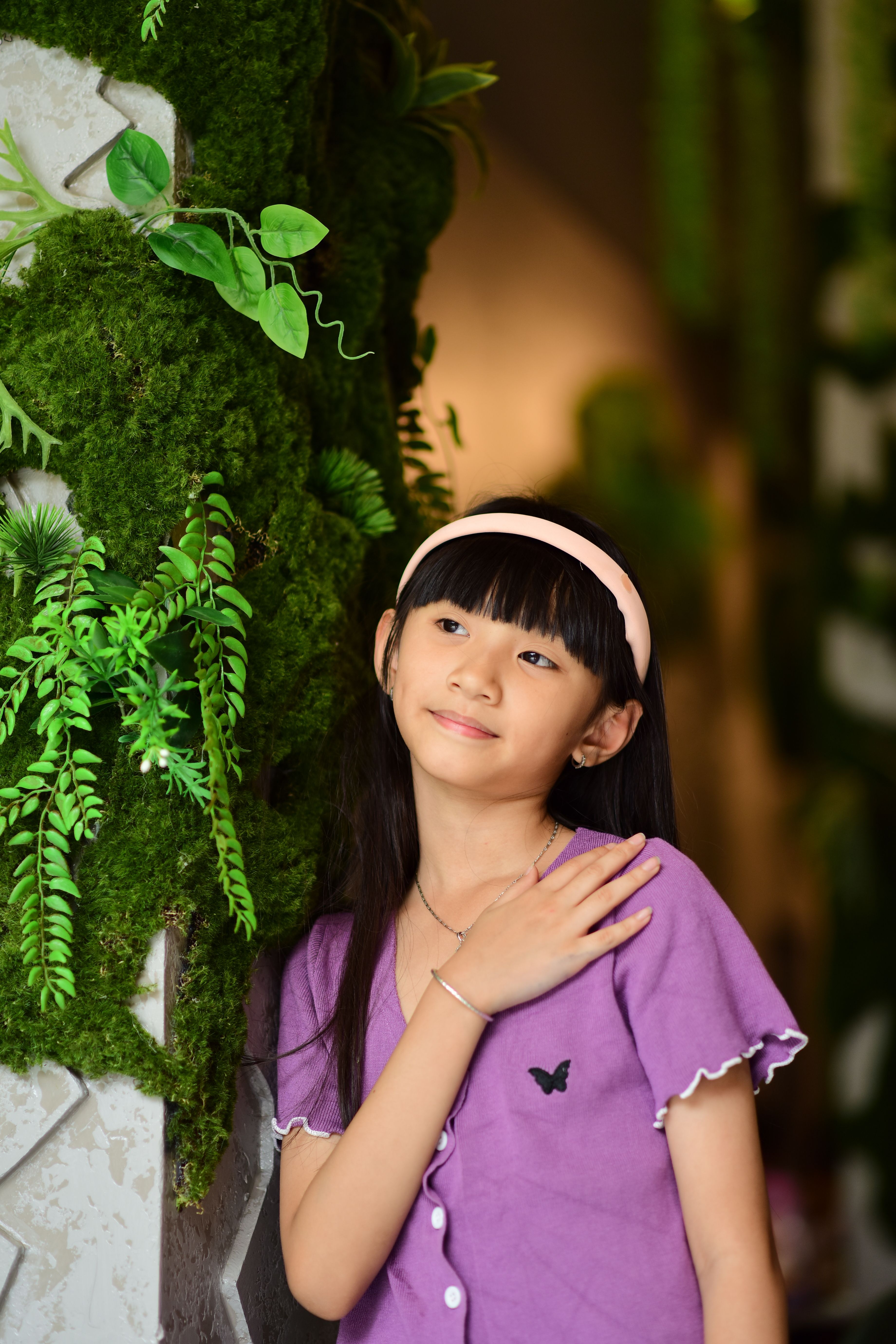 Young girl in a purple dress with plants in a cozy indoor setting.