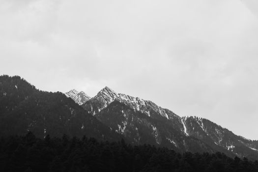 A striking black and white photo of a snowy mountain range under overcast skies.
