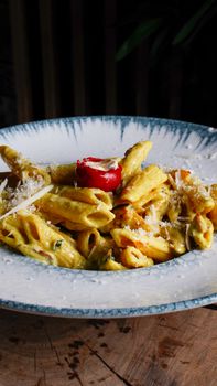 Savor a delicious plate of creamy penne pasta garnished with cheese and cherry tomato.