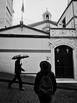 Black and white photo of people walking near a church in İstanbul, Türkiye on a rainy day.