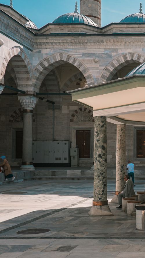 Free A peaceful moment in a historic mosque courtyard featuring stone arches and domed architecture. Stock Photo