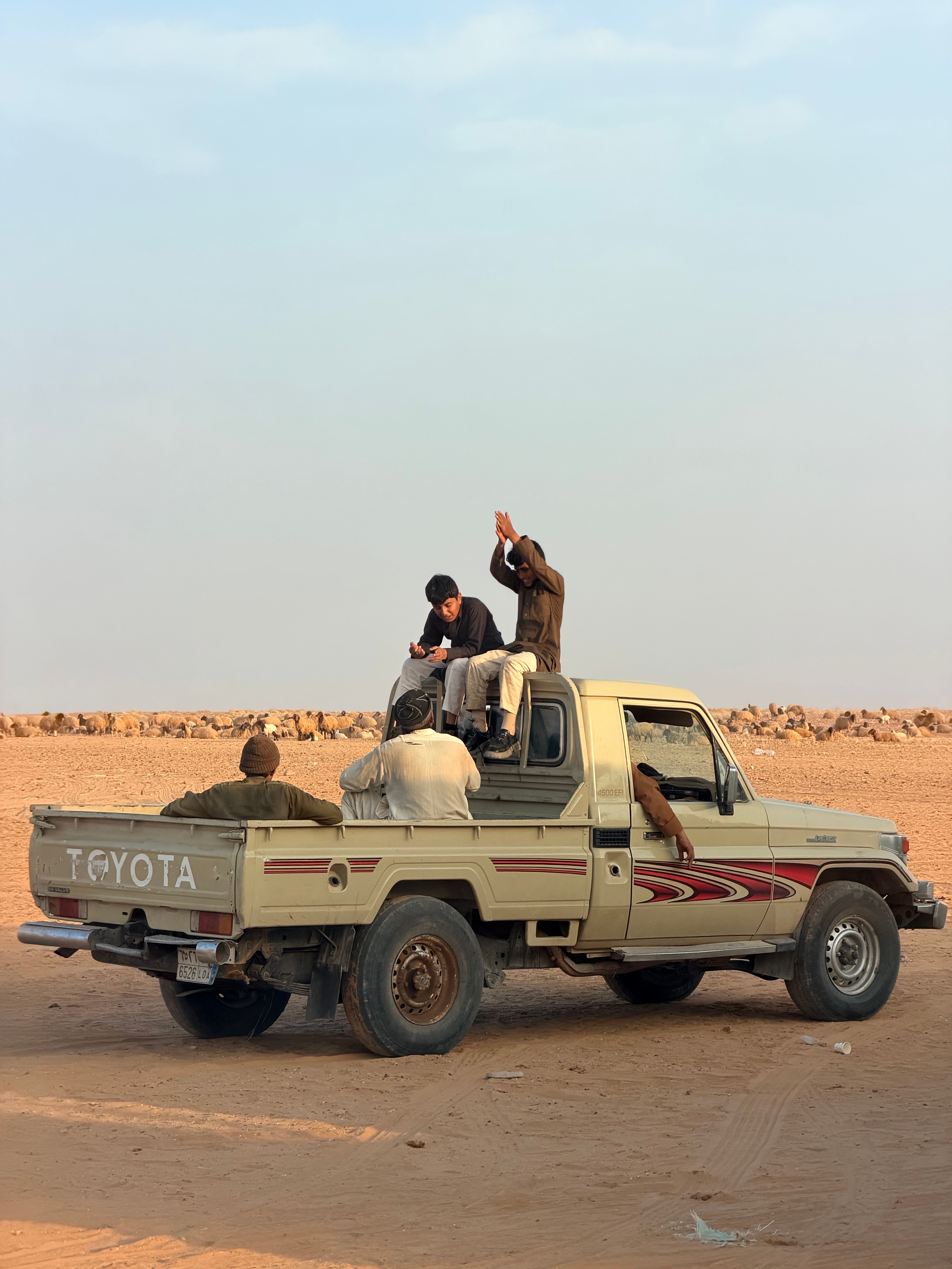 Four adults on a pickup truck in a vast desert landscape, enjoying the outdoors.
