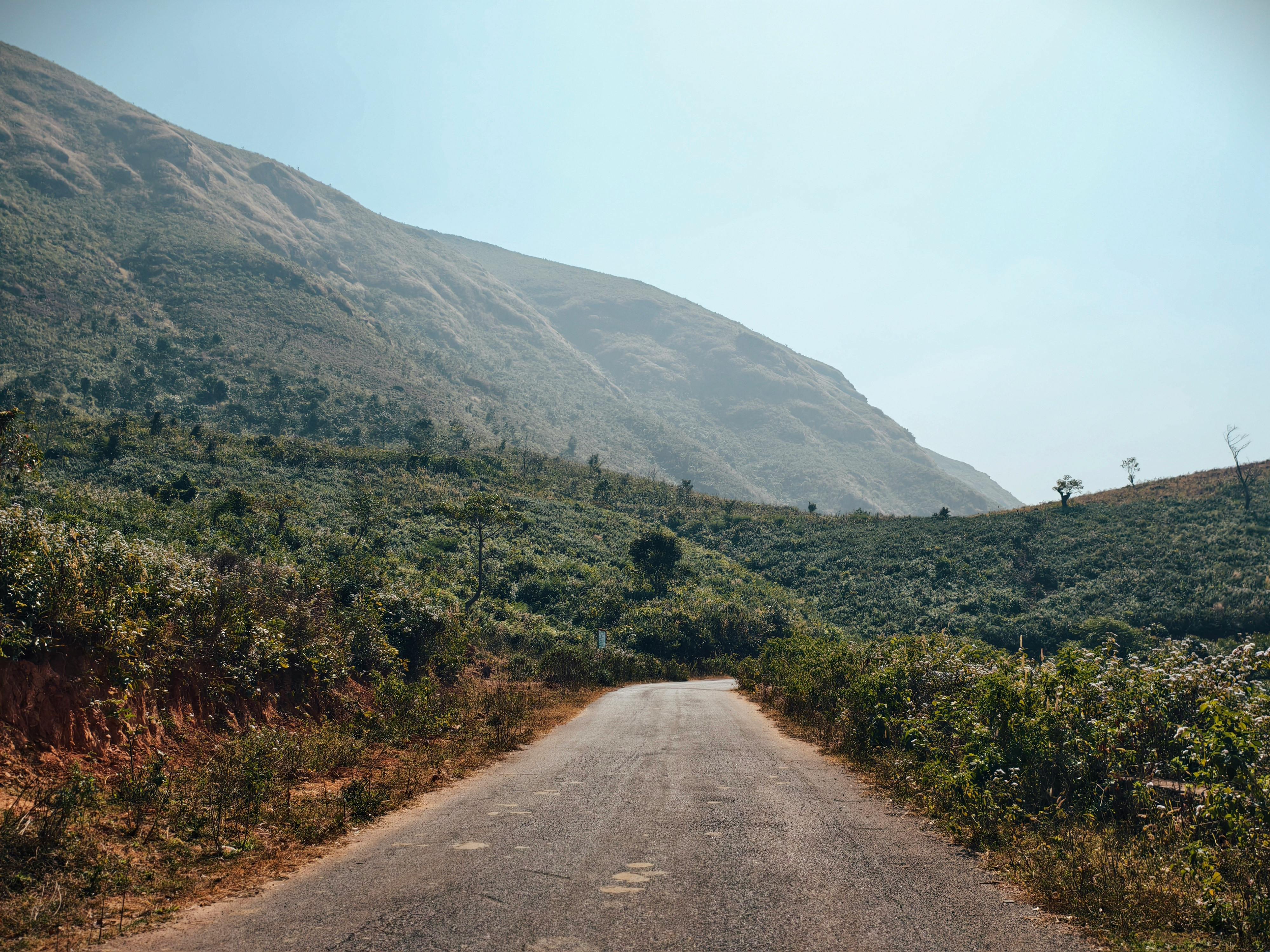 A peaceful road leading through lush green mountains under a clear blue sky.