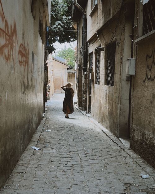 Free A woman in a hat walks through a narrow, cobblestone alley, exuding mystery. Stock Photo