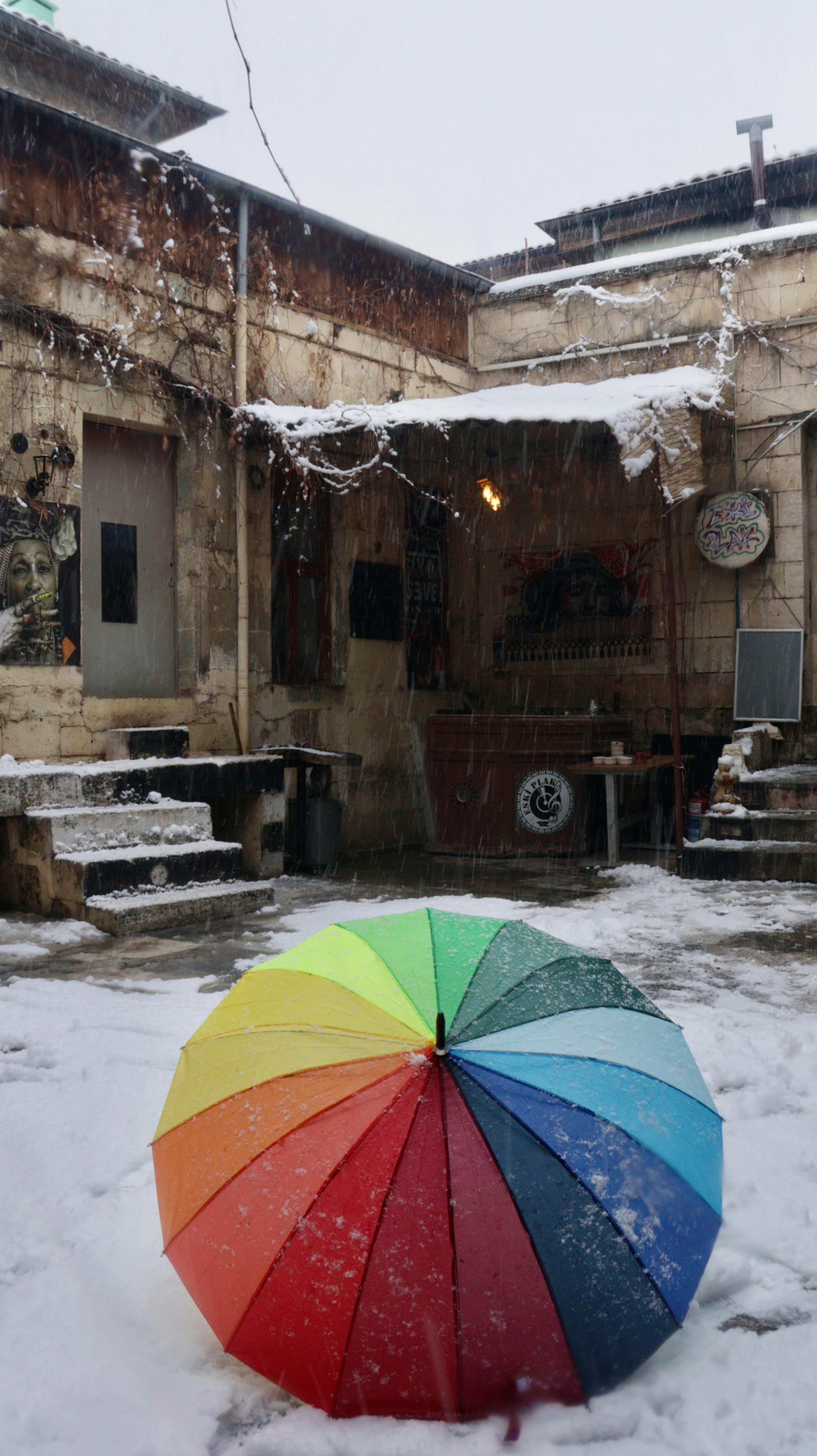 Vibrant rainbow umbrella in a rustic snowy courtyard, evokes contrast and mood.