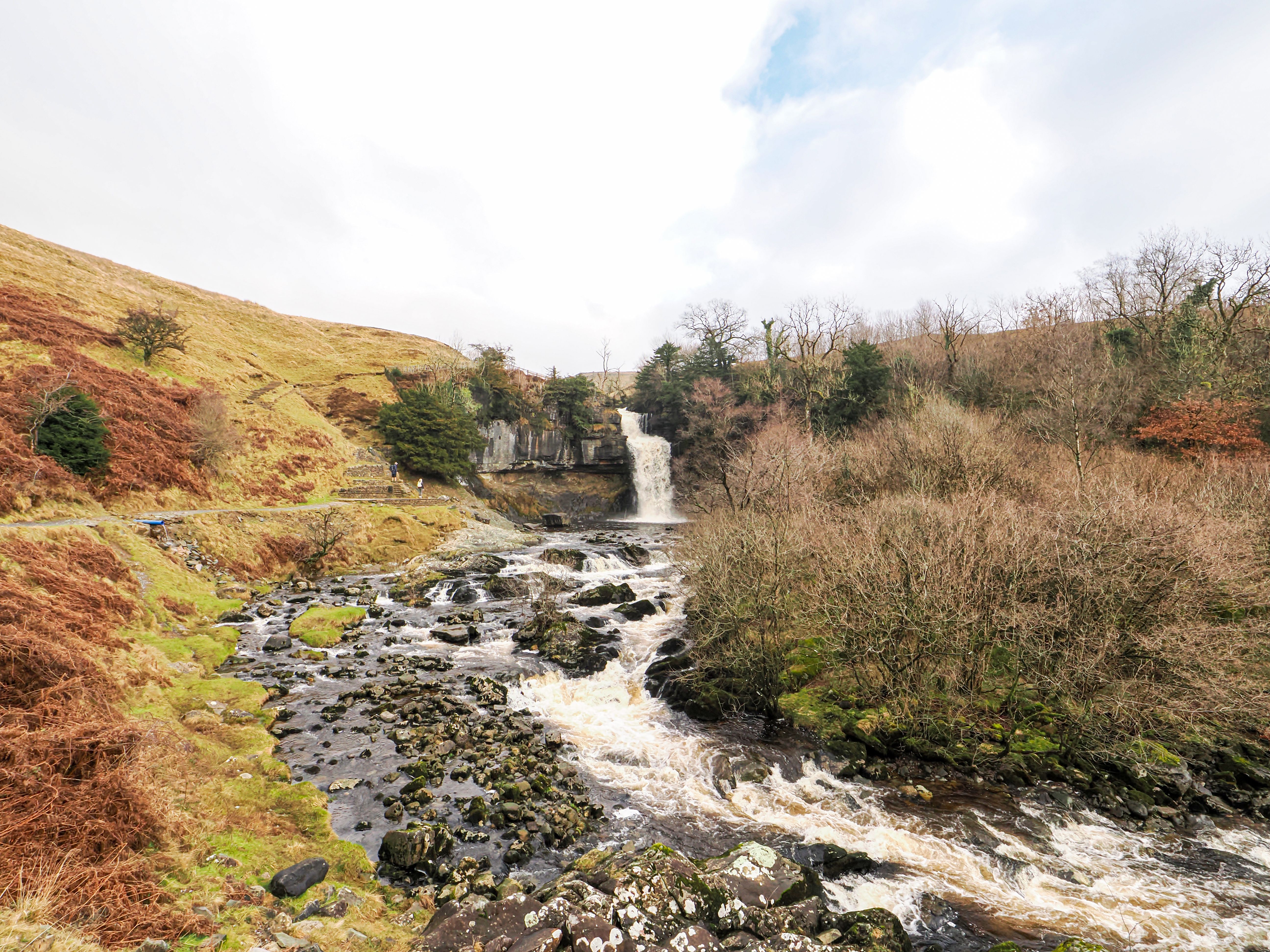 Stunning view of a waterfall in the Yorkshire Dales surrounded by lush greenery and rocky terrain.