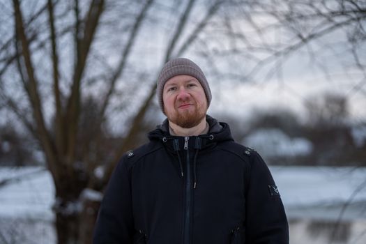 Adult male in winter attire standing outdoors with a snowy backdrop.