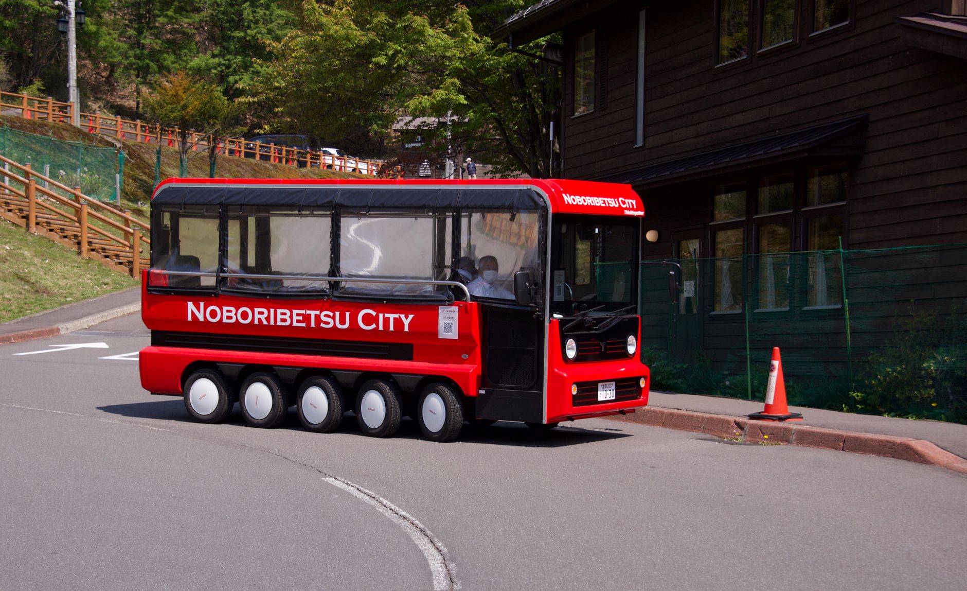 Red Noboribetsu City tourist bus traveling outdoors on a sunny day, showcasing local scenery and attractions.