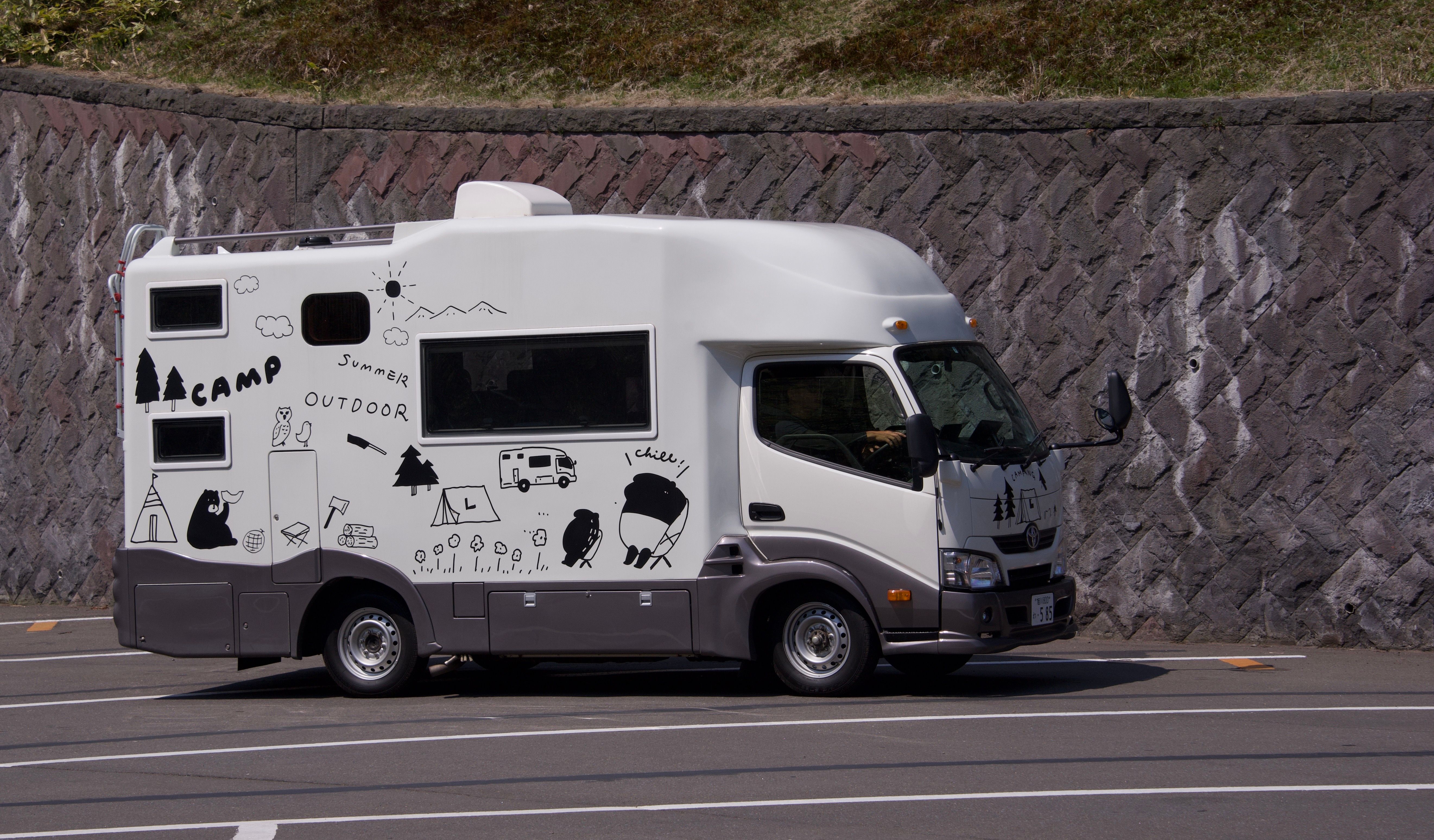 A quirky, illustration-covered camper van parked outdoors on a sunny day.