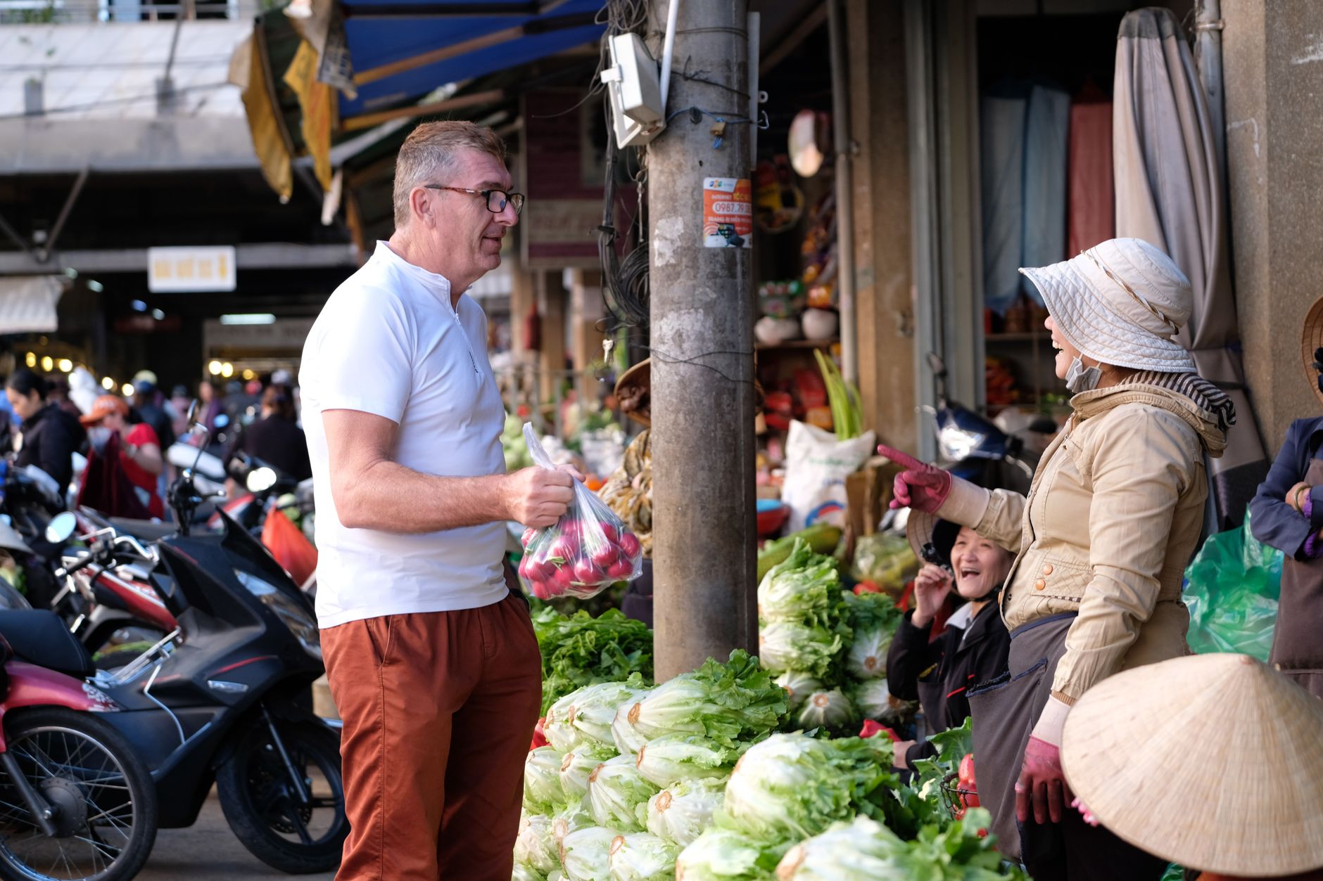 A vibrant scene at a bustling Vietnamese market with people interacting and fresh produce on display.