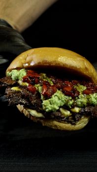 A close-up shot of a mouthwatering gourmet burger with toppings including guacamole and red peppers.