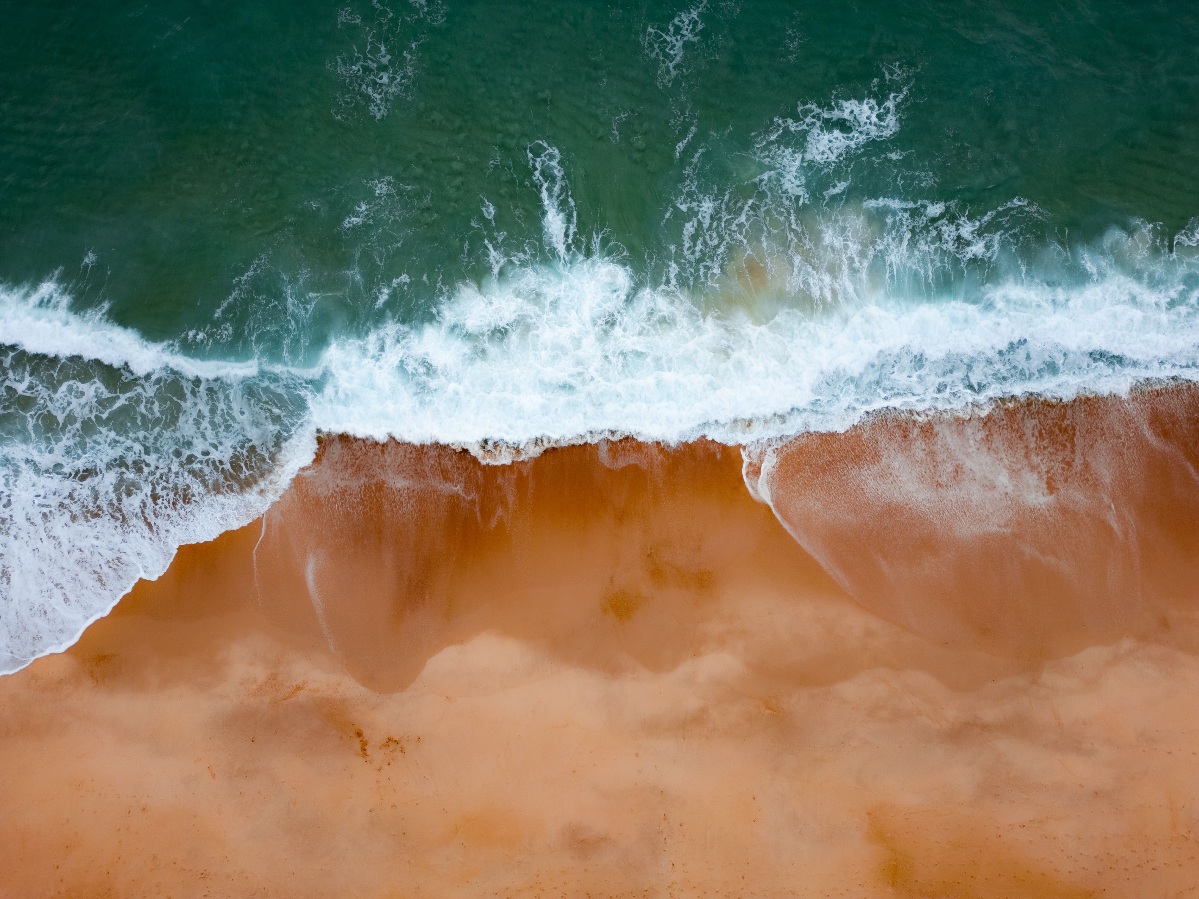 Gratis Fantastisk luftfoto av bølger som slår mot sandkysten ved Nazaré i Portugal. Arkivbilde