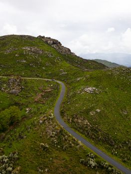 Scenic aerial view of a winding road through lush green hills and rocky terrain.