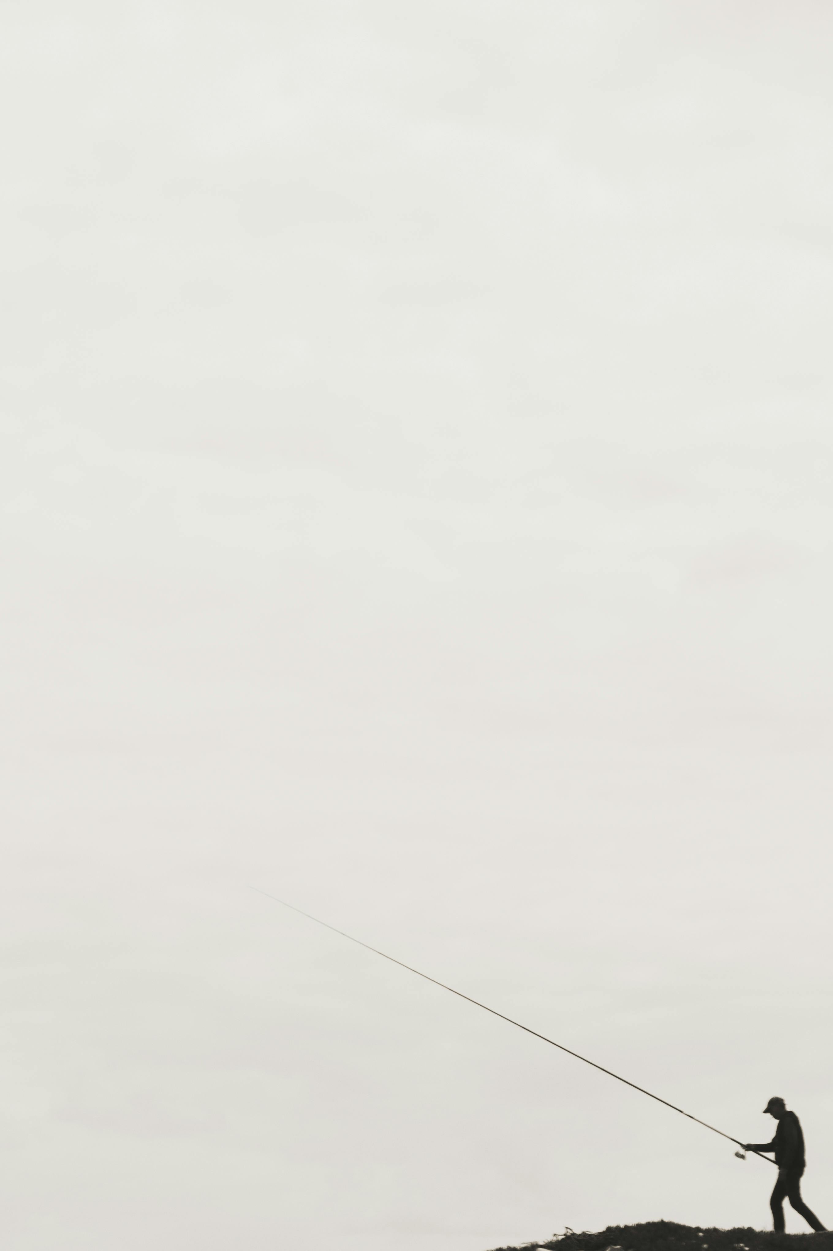 grátis Um pescador solitário lança sua linha contra um vasto céu nublado, personificando a solidão e o minimalismo. Foto profissional