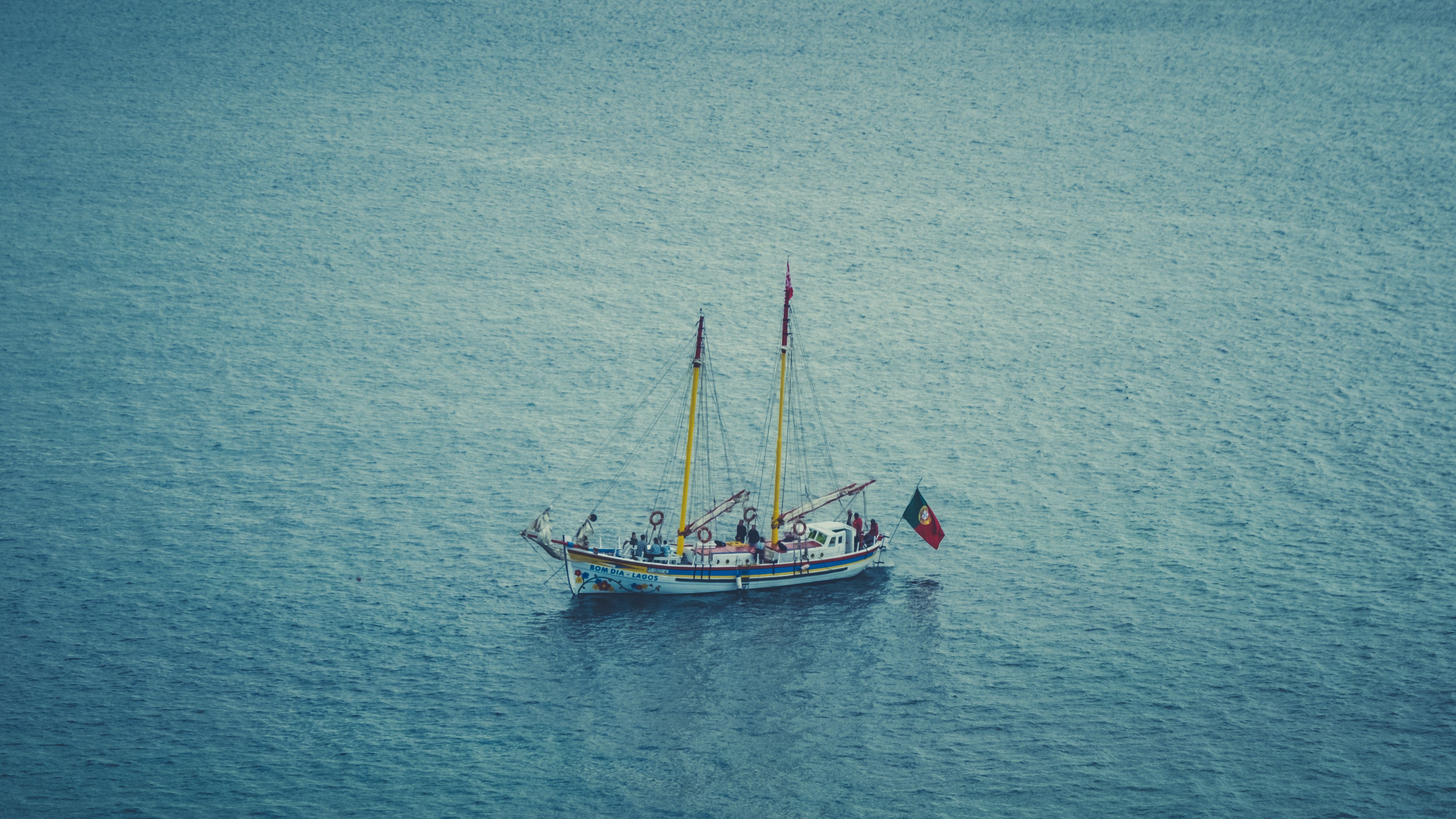 A sailing ship with a flag glides across the calm blue sea on a clear day.