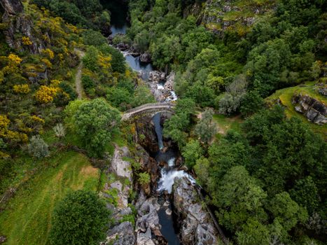 Aerial view of a stone bridge over a lush river gorge, surrounded by vibrant greenery.