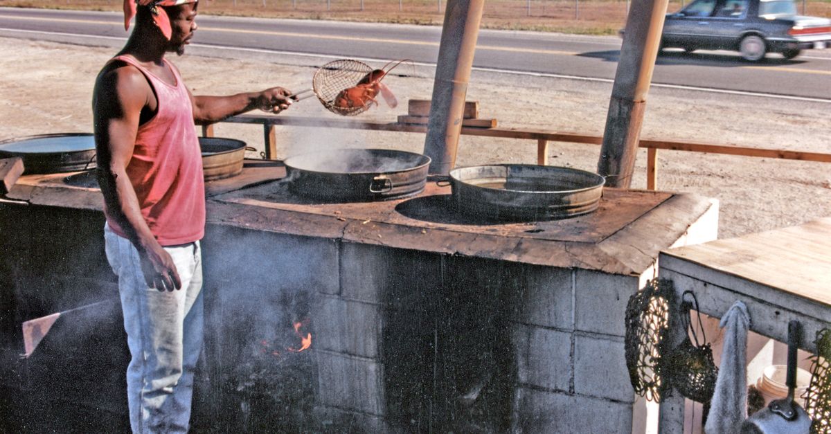 A man cooking Maine lobster outdoors by the roadside using traditional methods.
