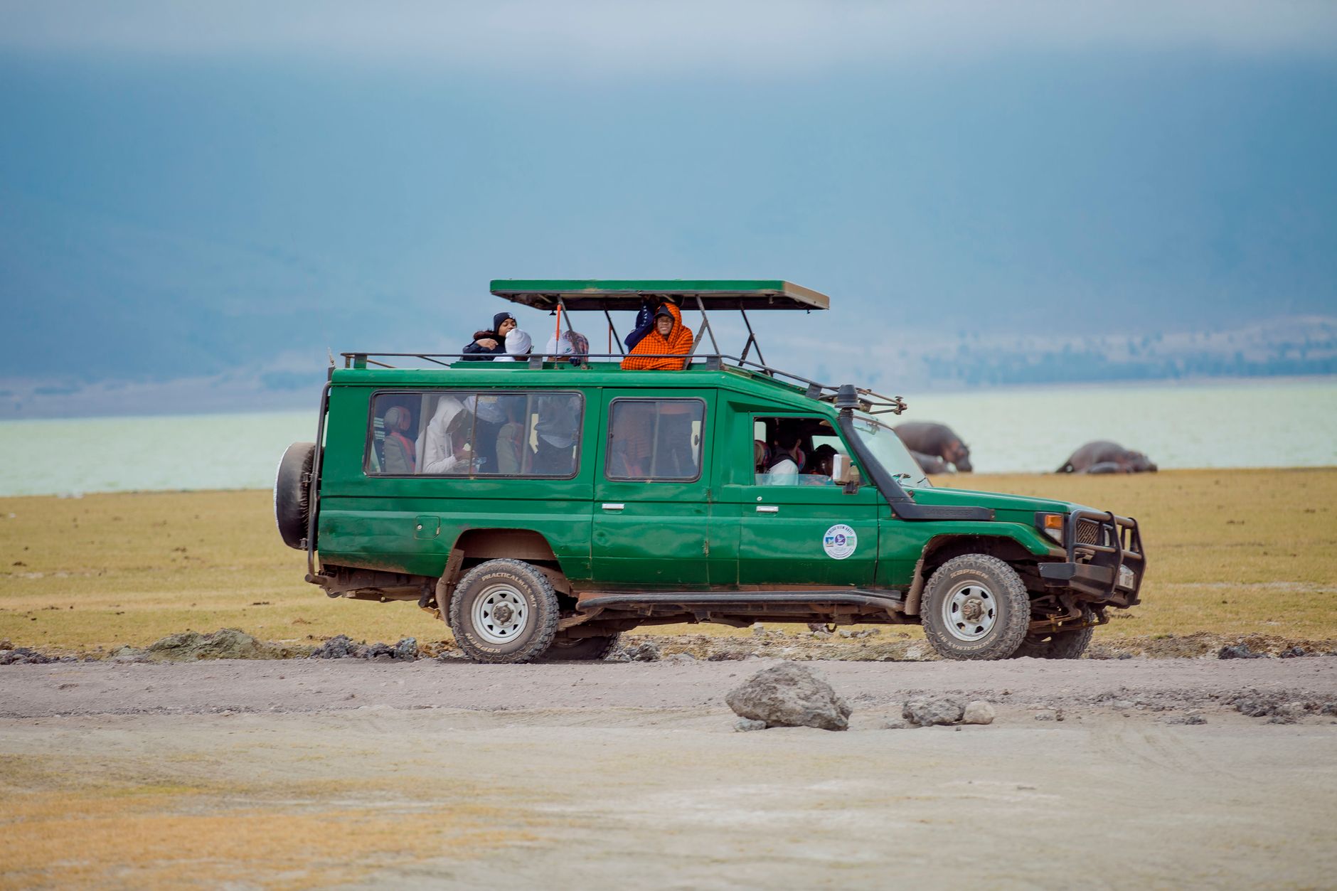 Tourists on a wildlife safari in a green jeep, exploring the vast African savanna under a clear sky.