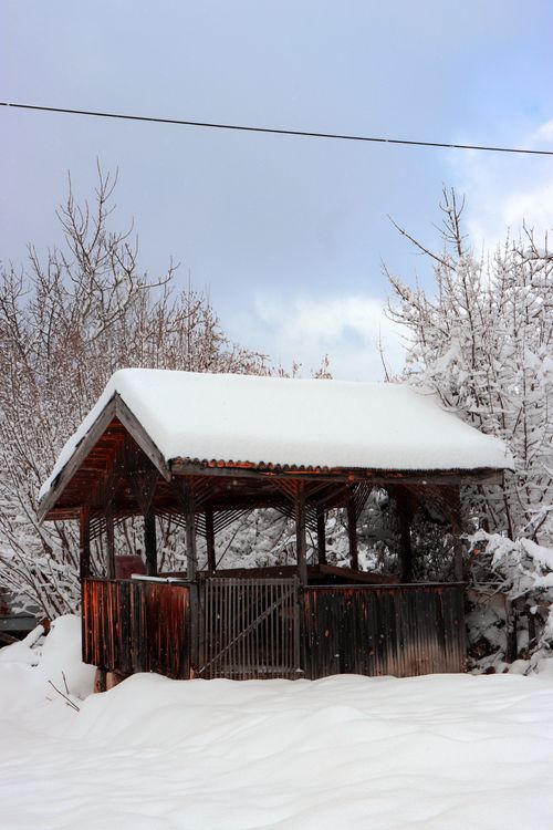 Free A wooden gazebo covered in snow, set in a tranquil winter landscape with white trees. Stock Photo