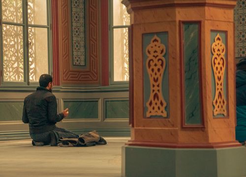 Free A man in contemplative prayer inside a richly decorated mosque interior. Stock Photo