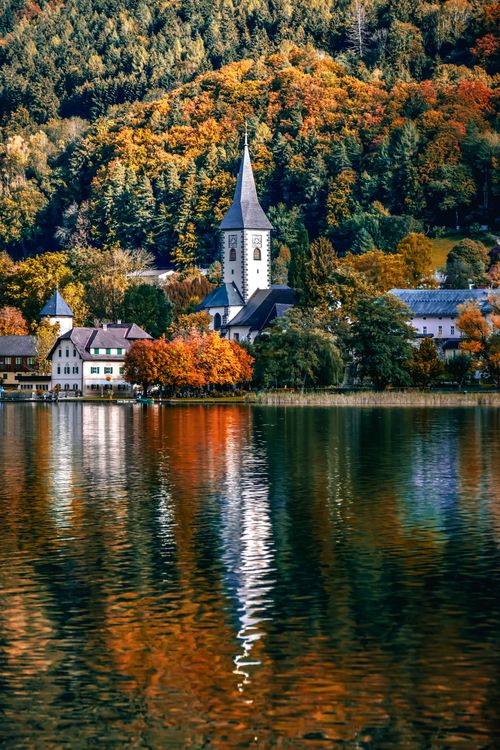 Free Picturesque village by a serene lake with colorful autumn foliage reflection in water. Stock Photo