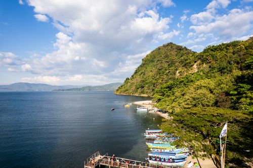 Free Discover the serene beauty of a tropical lake beside lush green mountains under a blue sky. Stock Photo