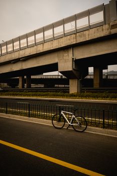 A single bicycle parked on a road beneath a large concrete bridge on a cloudy day.