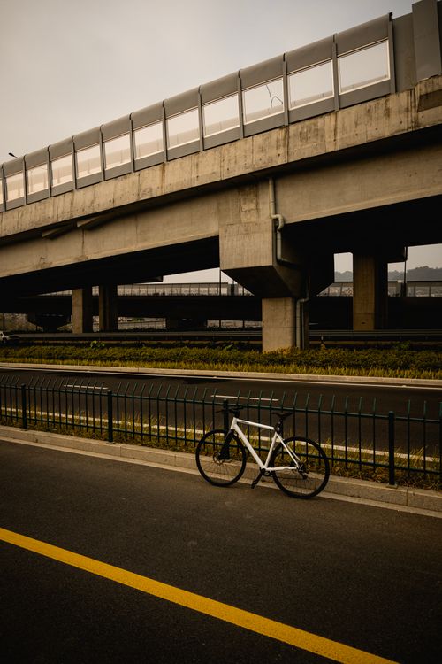 Free A single bicycle parked on a road beneath a large concrete bridge on a cloudy day. Stock Photo