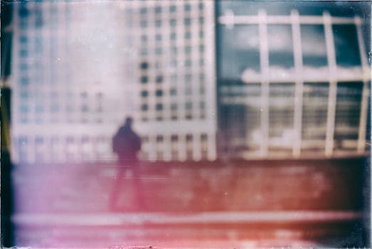 Blurred silhouette of a person against a glass building facade with artistic color effects.