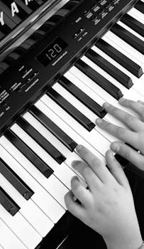 Close-up of a child's hands playing a piano keyboard in black and white.