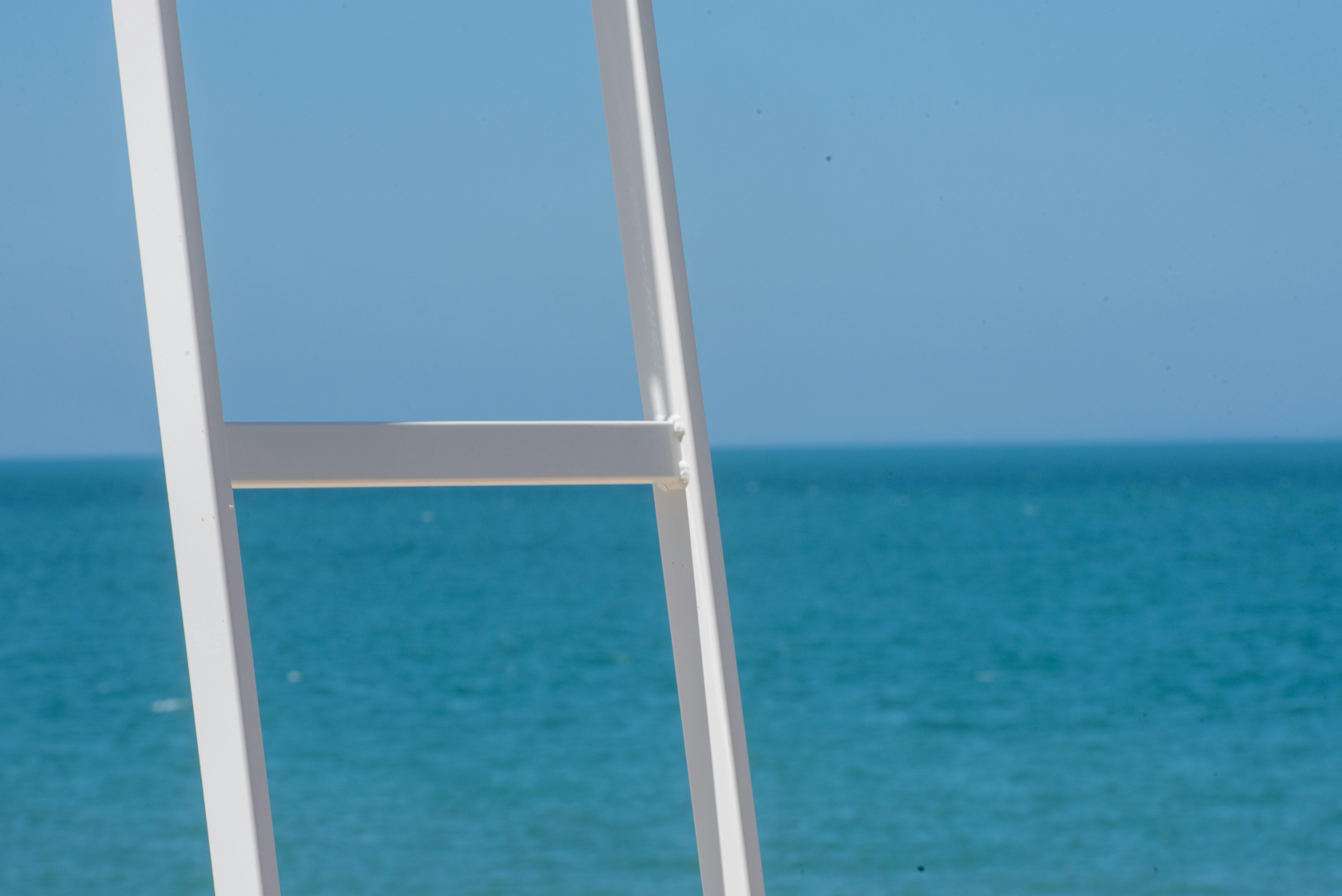 免费 一架白色的梯子矗立在湛蓝的大海和明媚的天空下。 素材图片