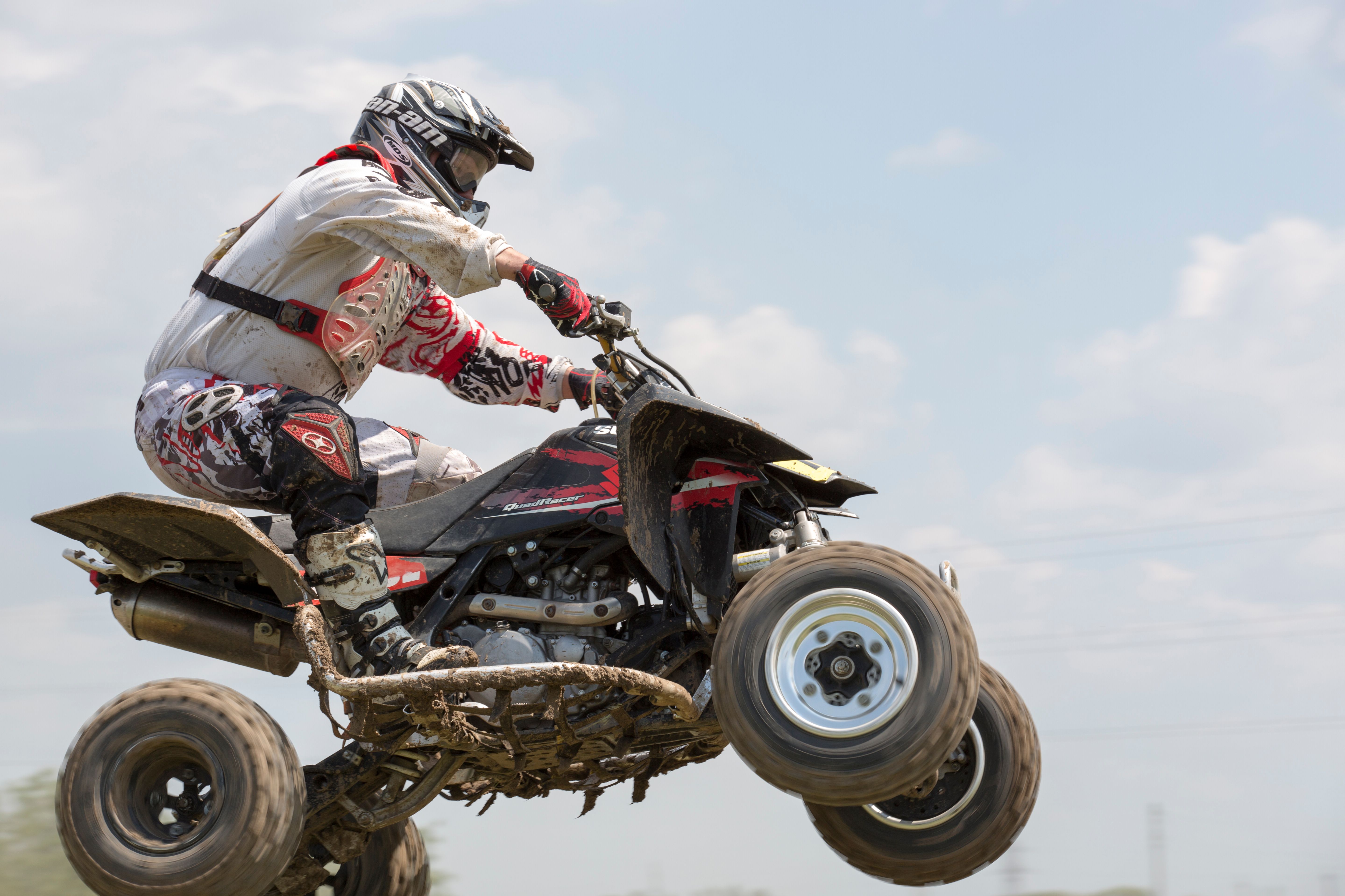 Dramatic action shot of an ATV rider airborne during a daytime outdoor race.