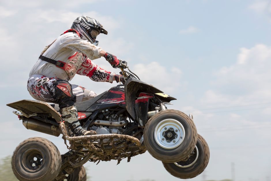 Dramatic action shot of an ATV rider airborne during a daytime outdoor race.