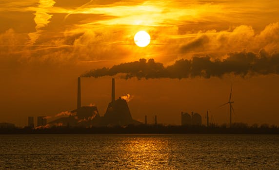 Dramatic skyline of a Copenhagen factory with smoke and wind turbines at sunset.