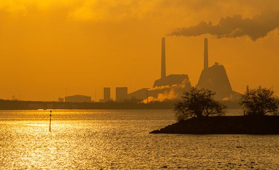 A striking silhouette of a power plant during sunset in Copenhagen, with vibrant orange tones reflected in the water.
