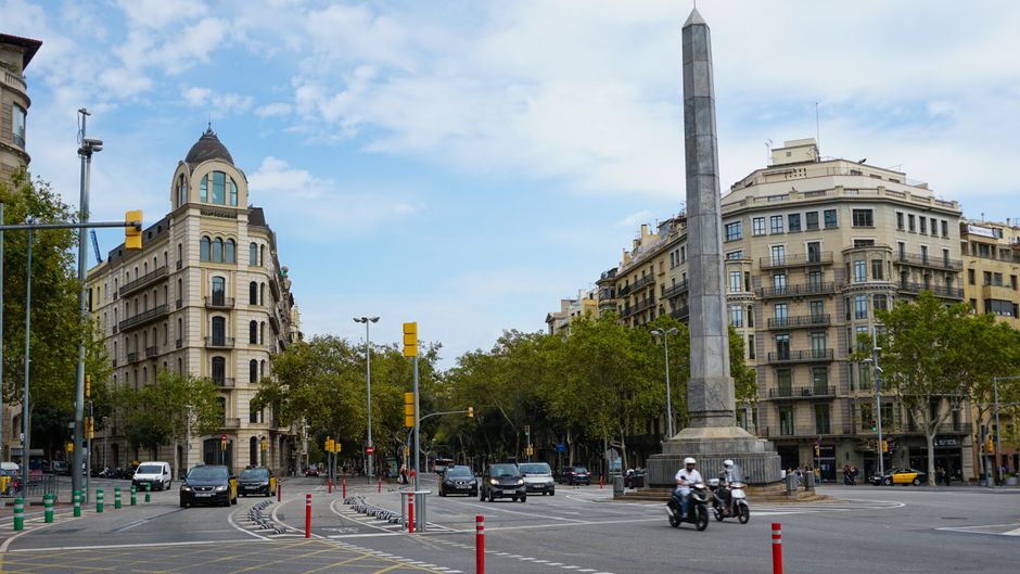 Escena urbana animada de Barcelona con tráfico y arquitectura histórica en un día soleado.