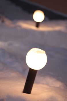 Close-up of glowing pathway lights illuminating snow-covered ground at night.